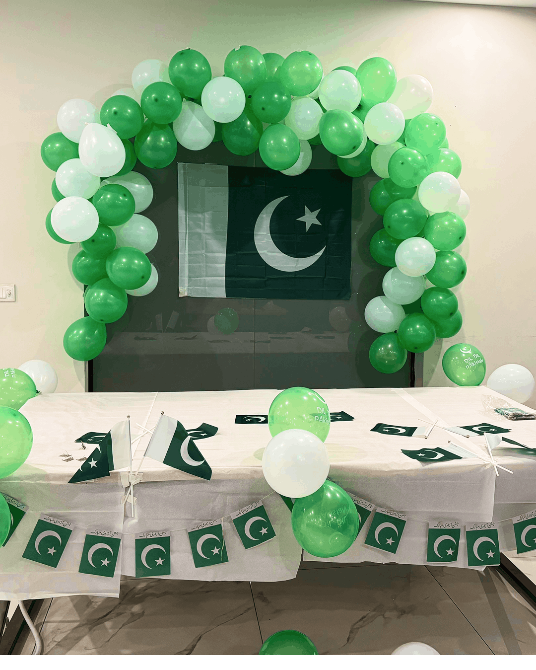 A green and white balloon arch framing the Pakistani flag, with festive table decorations
